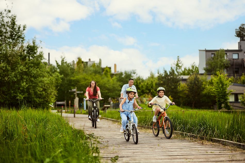 Une famille avec deux enfants font du vélo sur un chemin bordé de hautes herbes