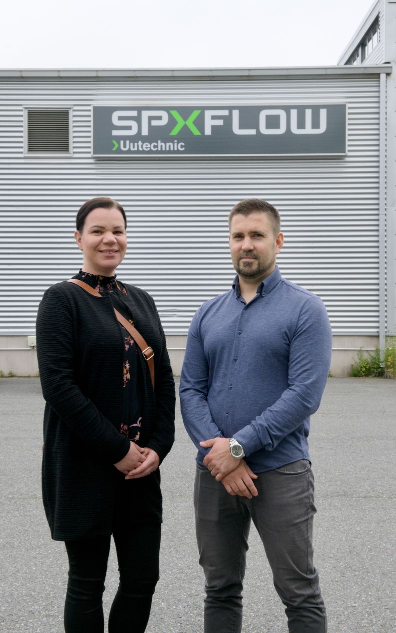 Nainen ja mies seisovat vierekkäin SPXFLOW Uutechnic -kyltin edessä.
