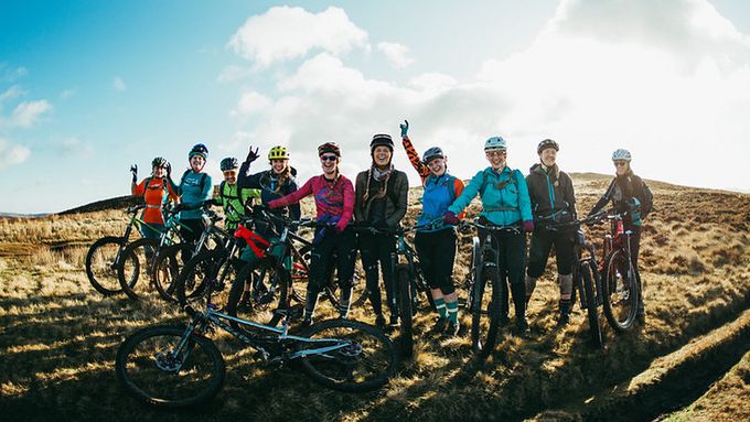 Group of a dozen women cyclists on a sunny hill smiling at camera