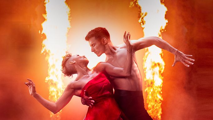 two dancers looking at each other with fire in the background