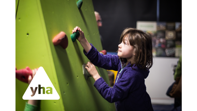 young girl in blue hoodie climbing an indoor climbing wall