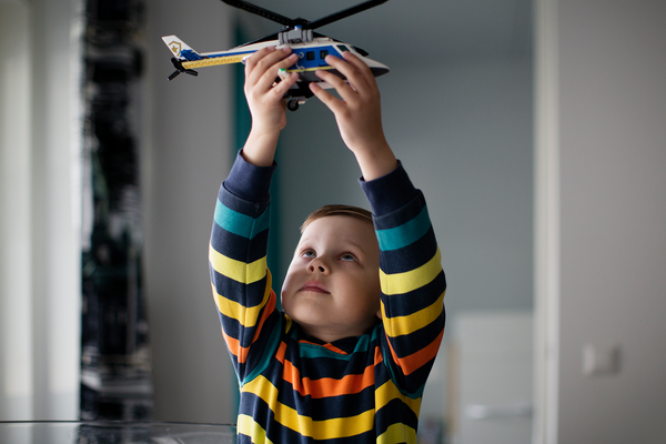 Kuvassa pieni poika monivärisessä raitapaidassa leikkii legohelikopterilla. Taustalla vaalea asunto.